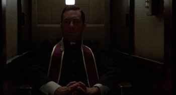 Movie still from “True Confessions” (1981), directed by Ulu Grosbard – A man sitting in a chair wearing a priest's outfit; Medium shot, Low angle
