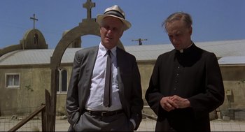Movie still from “True Confessions” (1981), directed by Ulu Grosbard – A man in a suit and a hat standing next to a woman in a priest's outfit; Medium shot, Low angle