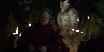 Movie still from “House of Cards” (2013), created by Beau Willimon – A man in a red robe standing in front of an animal; Medium shot, Over the shoulder angle