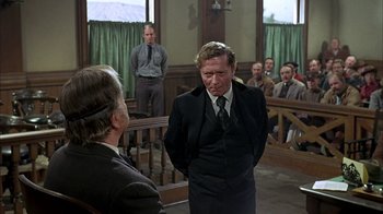 Movie still from “True Grit” (1969), directed by Henry Hathaway – A man in a suit and tie in front of a group of people; Medium shot, Over the shoulder angle