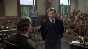 Movie still from “True Grit” (1969), directed by Henry Hathaway – A man in a suit and tie in front of a group of people; Medium shot, Over the shoulder angle