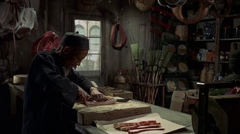 Movie still from “True Grit” (1969), directed by Henry Hathaway – A man cutting bacon on a cutting board in a kitchen; Medium shot, High angle