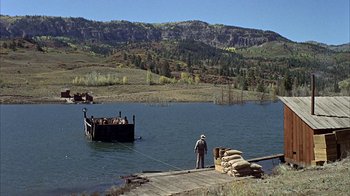 Movie still from “True Grit” (1969), directed by Henry Hathaway – A man standing on a dock next to a body of water; Extreme Wide shot, High angle