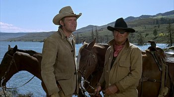 Movie still from “True Grit” (1969), directed by Henry Hathaway – Two men standing next to each other near a horse; Medium shot, Low angle