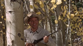Movie still from “True Grit” (1969), directed by Henry Hathaway – A man holding a rifle in a forest; Medium shot, Low angle