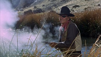Movie still from “True Grit” (1969), directed by Henry Hathaway – An old man in a cowboy hat is sitting by the water; Medium shot, Over the shoulder angle