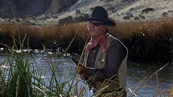 Movie still from “True Grit” (1969), directed by Henry Hathaway – A man wearing a cowboy hat and holding a fishing rod; Medium shot, Over the shoulder angle