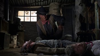 Movie still from “True Grit” (1969), directed by Henry Hathaway – A man kneeling down next to a dead body; Medium shot, Over the shoulder angle