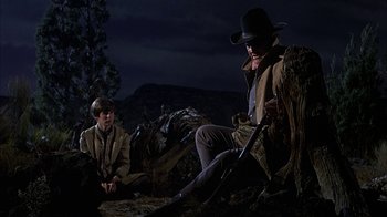 Movie still from “True Grit” (1969), directed by Henry Hathaway – A man sitting next to a boy holding a rifle; Medium shot, Low angle