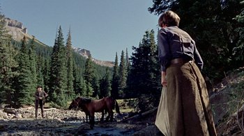Movie still from “True Grit” (1969), directed by Henry Hathaway – A woman standing next to a horse on a dirt road; Wide shot, Low angle