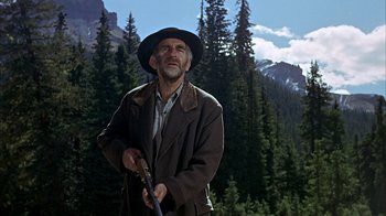Movie still from “True Grit” (1969), directed by Henry Hathaway – An old man holding a rifle in a wooded area; Medium shot, Low angle