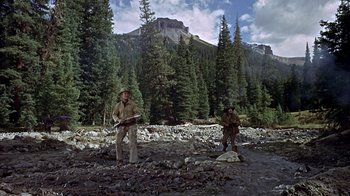 Movie still from “True Grit” (1969), directed by Henry Hathaway – Two men standing in a rocky area near a mountain; Wide shot, Low angle