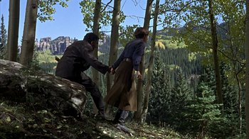 Movie still from “True Grit” (1969), directed by Henry Hathaway – A man and a woman holding hands while standing in the woods; Wide shot, High angle