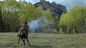 Movie still from “True Grit” (1969), directed by Henry Hathaway – A man riding a horse in a field with trees in the background; Wide shot, Low angle