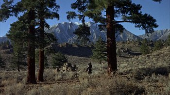 Movie still from “True Grit” (1969), directed by Henry Hathaway – A person standing in the middle of a field near trees and a mountain; Extreme Wide shot, Low angle