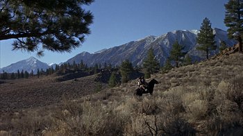 Movie still from “True Grit” (1969), directed by Henry Hathaway – A man riding a horse through a field with mountains in the background; Extreme Wide shot, Low angle