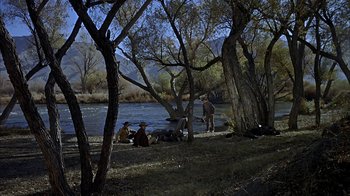 Movie still from “True Grit” (1969), directed by Henry Hathaway – A group of people sitting on the bank of a body of water; Wide shot, High angle