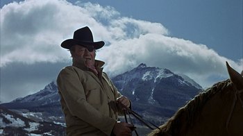 Movie still from “True Grit” (1969), directed by Henry Hathaway – A man wearing a cowboy hat while standing on a horse; Medium shot, Low angle