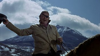 Movie still from “True Grit” (1969), directed by Henry Hathaway – An older man riding a horse in front of a mountain range; Medium shot, Low angle