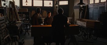 Movie still from “True Grit” (2010), directed by Ethan Coen – A group of people standing around a table; Wide shot, Over the shoulder angle