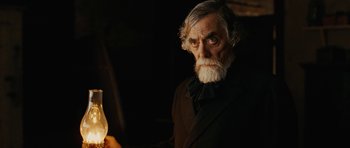 Movie still from “True Grit” (2010), directed by Ethan Coen – An old man with a beard and mustache holding a lit candle; Close Up shot, Over the shoulder angle