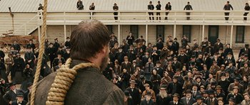 Movie still from “True Grit” (2010), directed by Ethan Coen – A crowd of people standing in front of a building; Wide shot, Over the shoulder angle