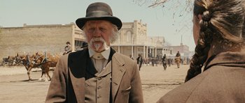 Movie still from “True Grit” (2010), directed by Ethan Coen – An old man with a beard wearing a suit and a hat; Close Up shot, Over the shoulder angle