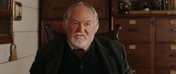 Movie still from “True Grit” (2010), directed by Ethan Coen – An older man with a beard and a suit; Close Up shot, Over the shoulder angle