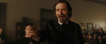 Movie still from “True Grit” (2010), directed by Ethan Coen – A man with long hair and a beard wearing a suit and tie; Close Up shot, Over the shoulder angle
