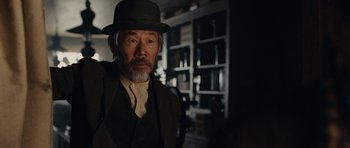 Movie still from “True Grit” (2010), directed by Ethan Coen – An older man wearing a hat in a dark room; Close Up shot, Over the shoulder angle