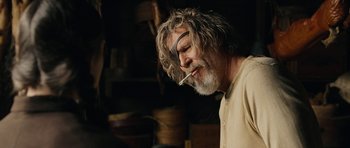 Movie still from “True Grit” (2010), directed by Ethan Coen – An older man smoking a cigarette in a room; Close Up shot, Over the shoulder angle