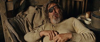 Movie still from “True Grit” (2010), directed by Ethan Coen – An old man with a beard and eye patch smoking a cigarette; Medium shot, Low angle