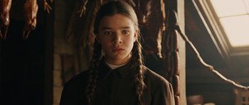 Movie still from “True Grit” (2010), directed by Ethan Coen – A young girl with plaited pigtails stands in front of a wall; Close Up shot, Low angle
