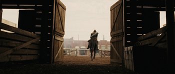 Movie still from “True Grit” (2010), directed by Ethan Coen – A man riding a horse through a gate; Wide shot, Over the shoulder angle
