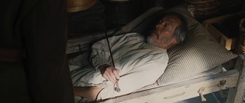 Movie still from “True Grit” (2010), directed by Ethan Coen – An old man laying in a bed with a cane; Medium shot, High angle