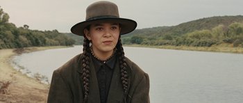 Movie still from “True Grit” (2010), directed by Ethan Coen – A woman with braids and a hat standing in front of a body of water; Close Up shot, Low angle