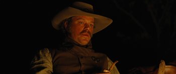 Movie still from “True Grit” (2010), directed by Ethan Coen – A man in a cowboy hat holding a pipe; Close Up shot, Over the shoulder angle