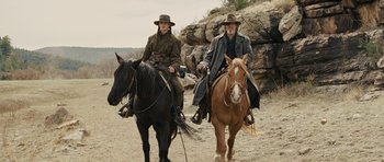 Movie still from “True Grit” (2010), directed by Ethan Coen – Two people riding horses on a dirt road; Wide shot, Low angle