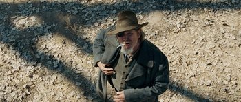 Movie still from “True Grit” (2010), directed by Ethan Coen – An old man with a beard and a hat is smoking a cigarette; Medium shot, Low angle