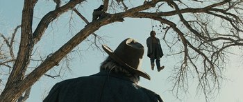 Movie still from “True Grit” (2010), directed by Ethan Coen – A man in a hat is looking up at a hanged man; Wide shot, Low angle