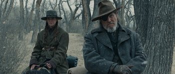 Movie still from “True Grit” (2010), directed by Ethan Coen – A man and a woman sitting on a bench in the snow; Medium shot, Over the shoulder angle