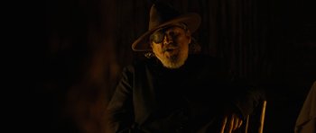 Movie still from “True Grit” (2010), directed by Ethan Coen – A man wearing a hat and sunglasses in the dark; Close Up shot, Over the shoulder angle