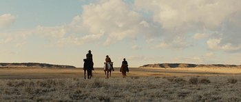 Movie still from “True Grit” (2010), directed by Ethan Coen – A group of people riding horses across a dry grass field; Extreme Wide shot, Low angle