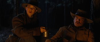 Movie still from “True Grit” (2010), directed by Ethan Coen – A man and a woman sitting next to each other in the dark; Medium shot, Low angle