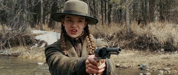 Movie still from “True Grit” (2010), directed by Ethan Coen – A young woman holding a gun while standing in the woods; Close Up shot, Low angle