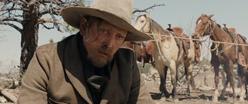 Movie still from “True Grit” (2010), directed by Ethan Coen – A man in a cowboy hat sitting in front of a horse; Close Up shot, Low angle