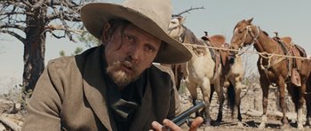 Movie still from “True Grit” (2010), directed by Ethan Coen – A man with a gun in his hand and two horses in the background; Close Up shot, Over the shoulder angle
