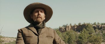 Movie still from “True Grit” (2010), directed by Ethan Coen – A man wearing a cowboy hat standing in front of a mountain; Close Up shot, Low angle