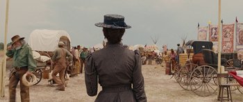 Movie still from “True Grit” (2010), directed by Ethan Coen – A woman wearing a hat standing in front of a crowd; Wide shot, Over the shoulder angle