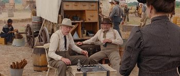 Movie still from “True Grit” (2010), directed by Ethan Coen – Two men sitting next to each other in front of an antique trunk; Medium shot, Over the shoulder angle